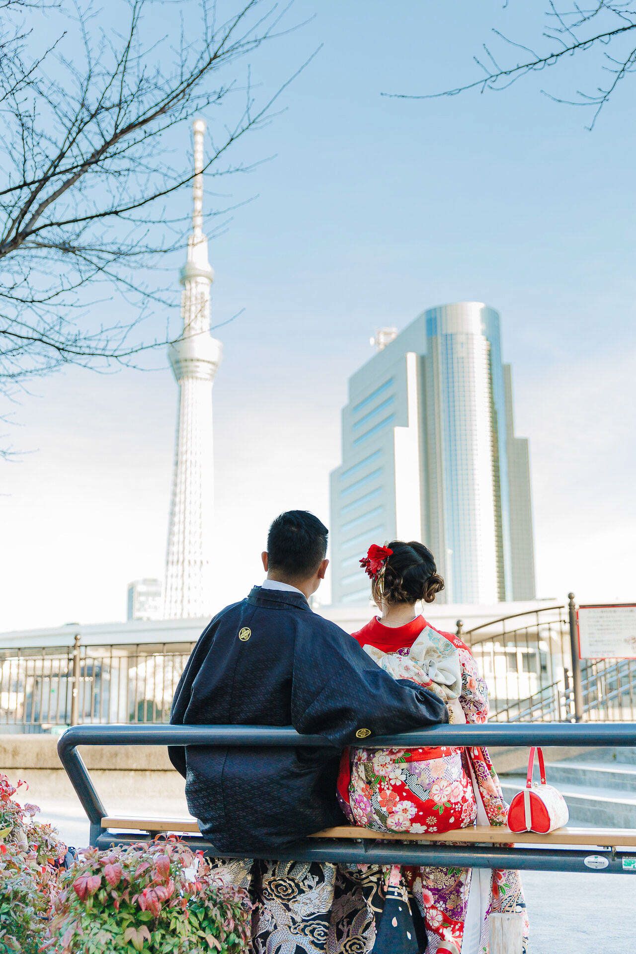 A couple in traditional Japanese attire sits on a bench overlooking the Tokyo Skytree tower.