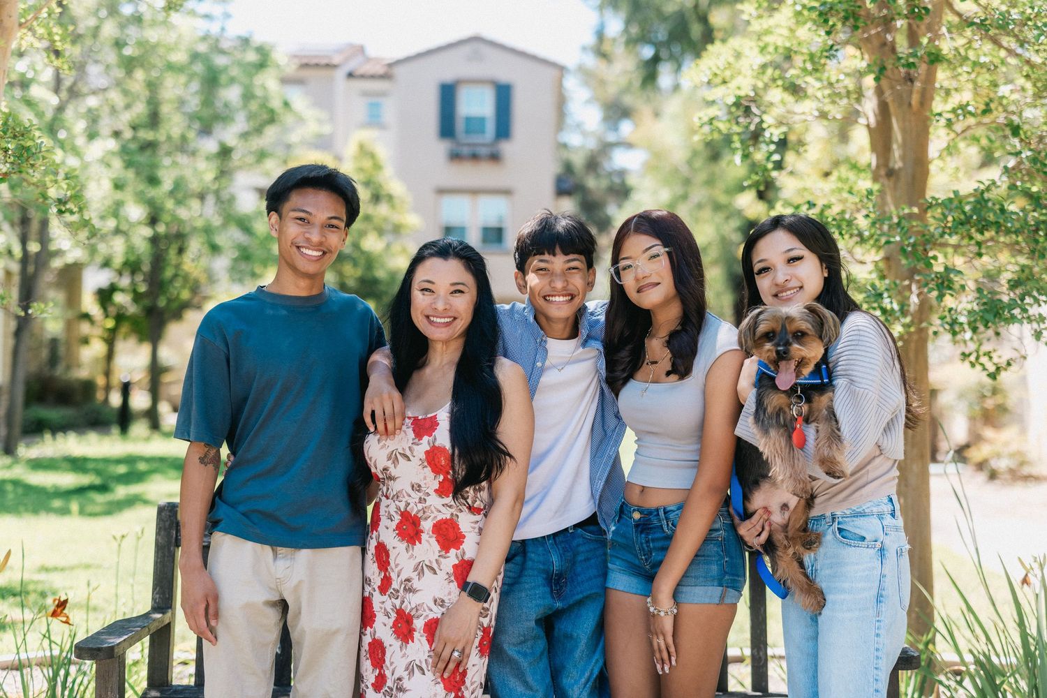 Group of friends pose together outdoors with trees and a building in the background.