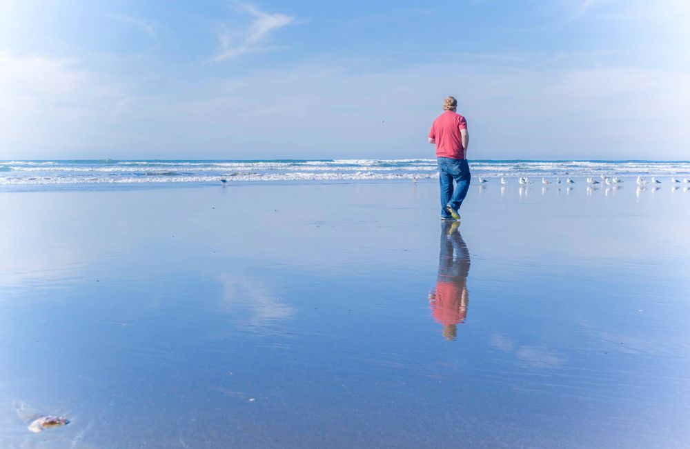 Silhouette of person walking on reflective beach at sunset.
