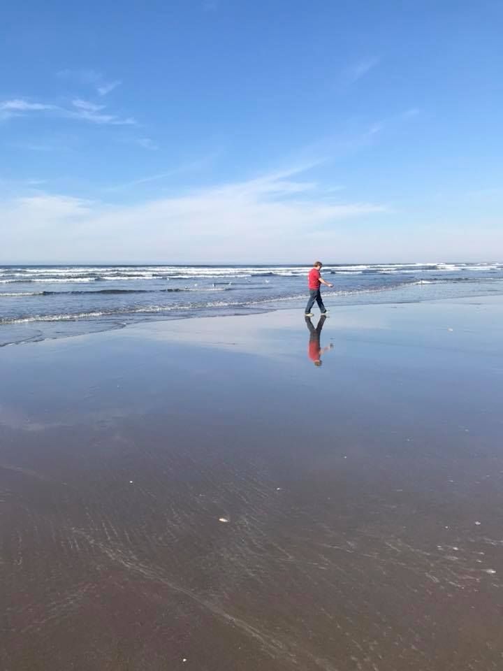 Figure in red jacket walking along empty beach with waves.