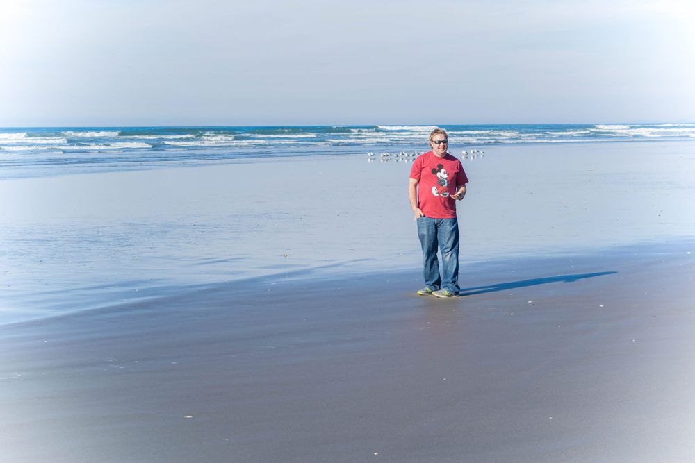 Lone figure walking along misty ocean shoreline wearing red jacket.