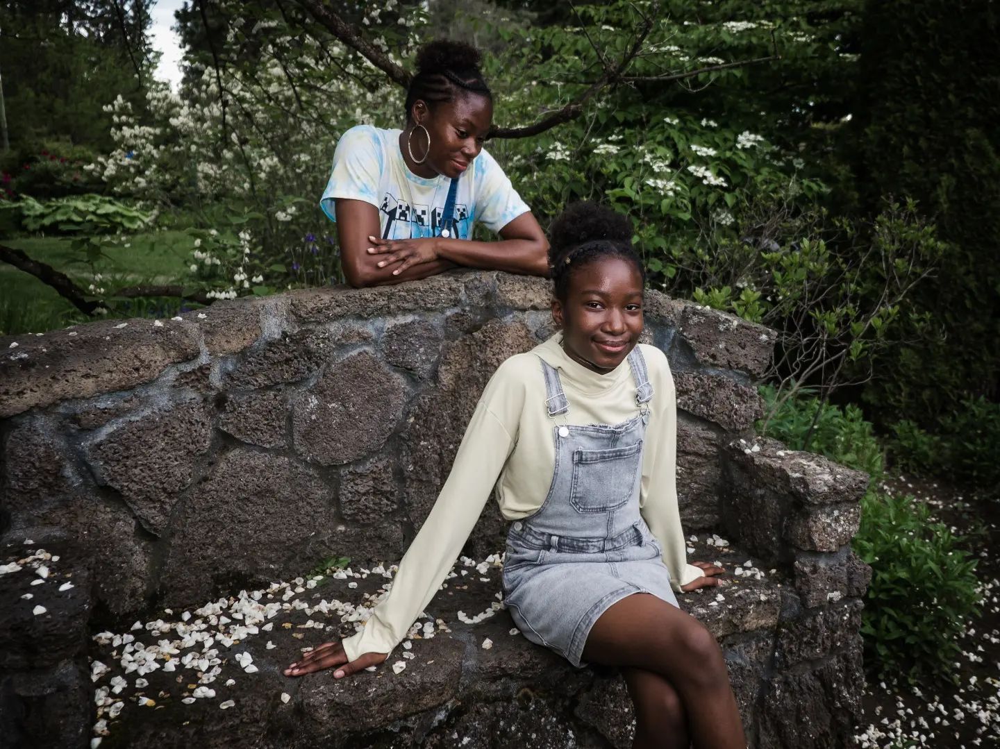 Two people relaxing on a stone wall surrounded by nature and small white flowers. Family Photography