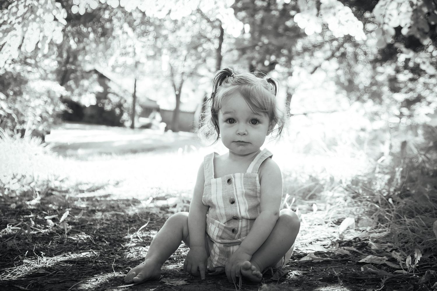 Black and white portrait of small child sitting outdoors in natural lighting.