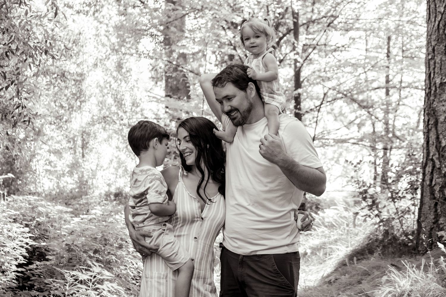 Black and white family portrait captured in forest setting with natural lighting.