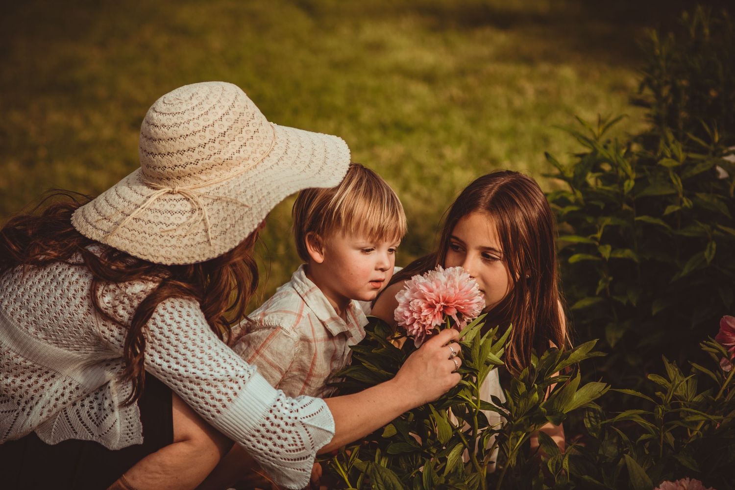 Three people sharing a tender moment smelling flowers in a garden setting. Family Photography