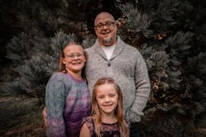A family group poses together in front of evergreen trees wearing cozy sweaters.