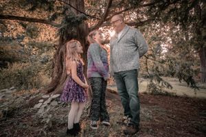 A family group poses together outdoors under autumn trees in casual clothing.