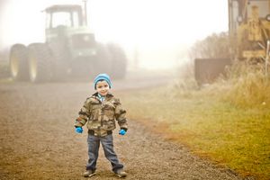 Small child in winter clothing stands in a misty field with a tractor silhouette in the background.
