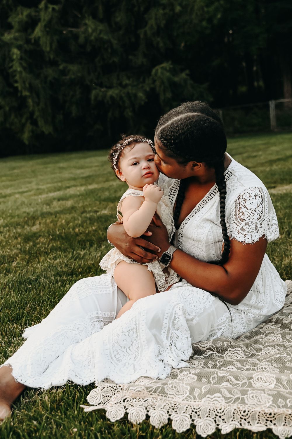 A tender moment captured outdoors with white lace dresses against a green background.