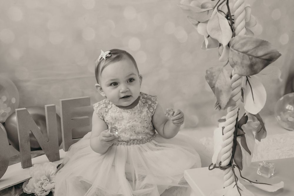 A series of black and white photos showing a baby in a dress during a cake smash session.