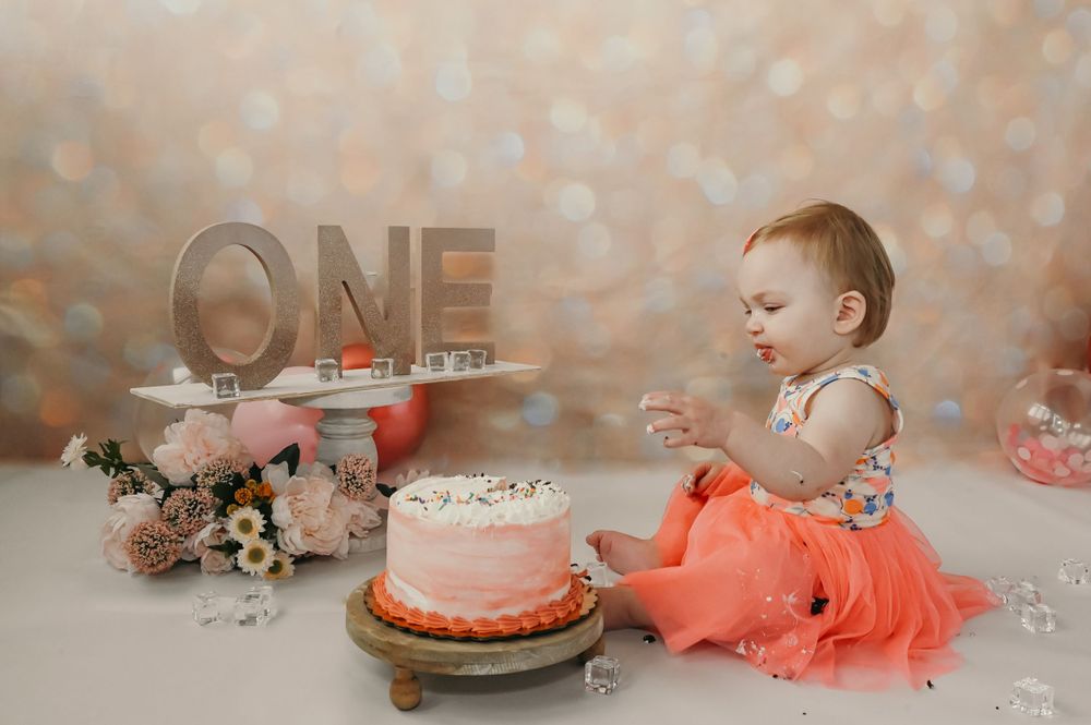 A cake smash photo session setup with pink decorations and 'ONE' lettering.