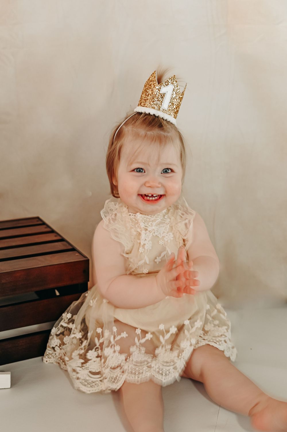 Baby wearing lace dress and crown smiles during first birthday photoshoot.
