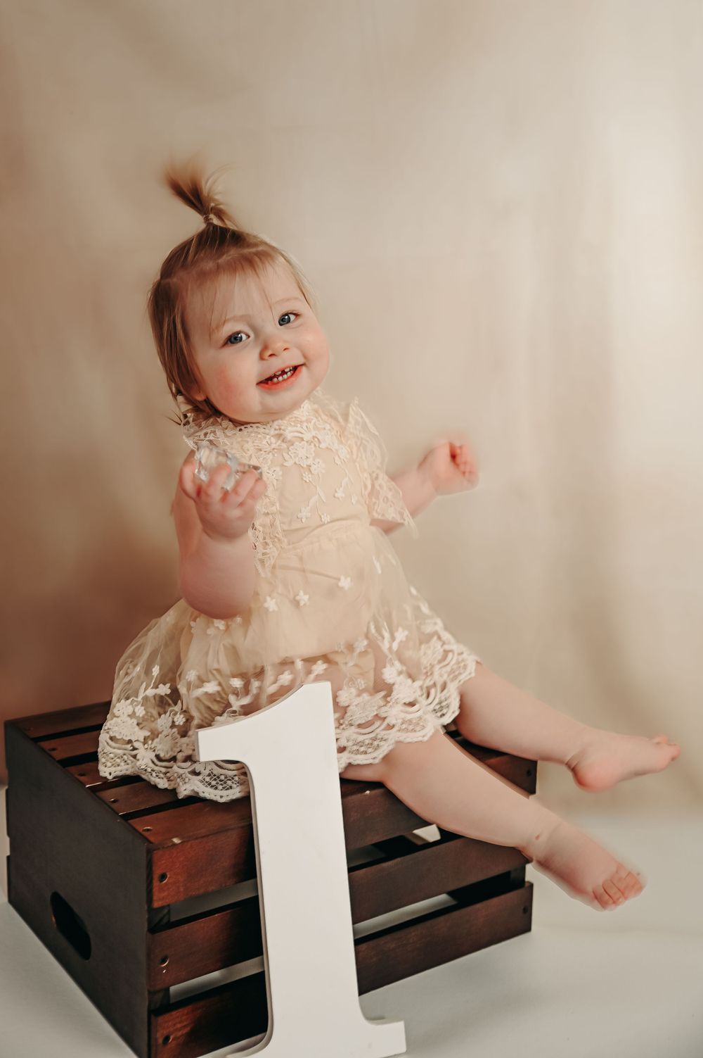 Baby in lace dress poses on wooden bench during first birthday photo session.