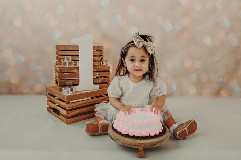 First birthday portrait with pink cake and wooden crate decorations against sparkly backdrop.