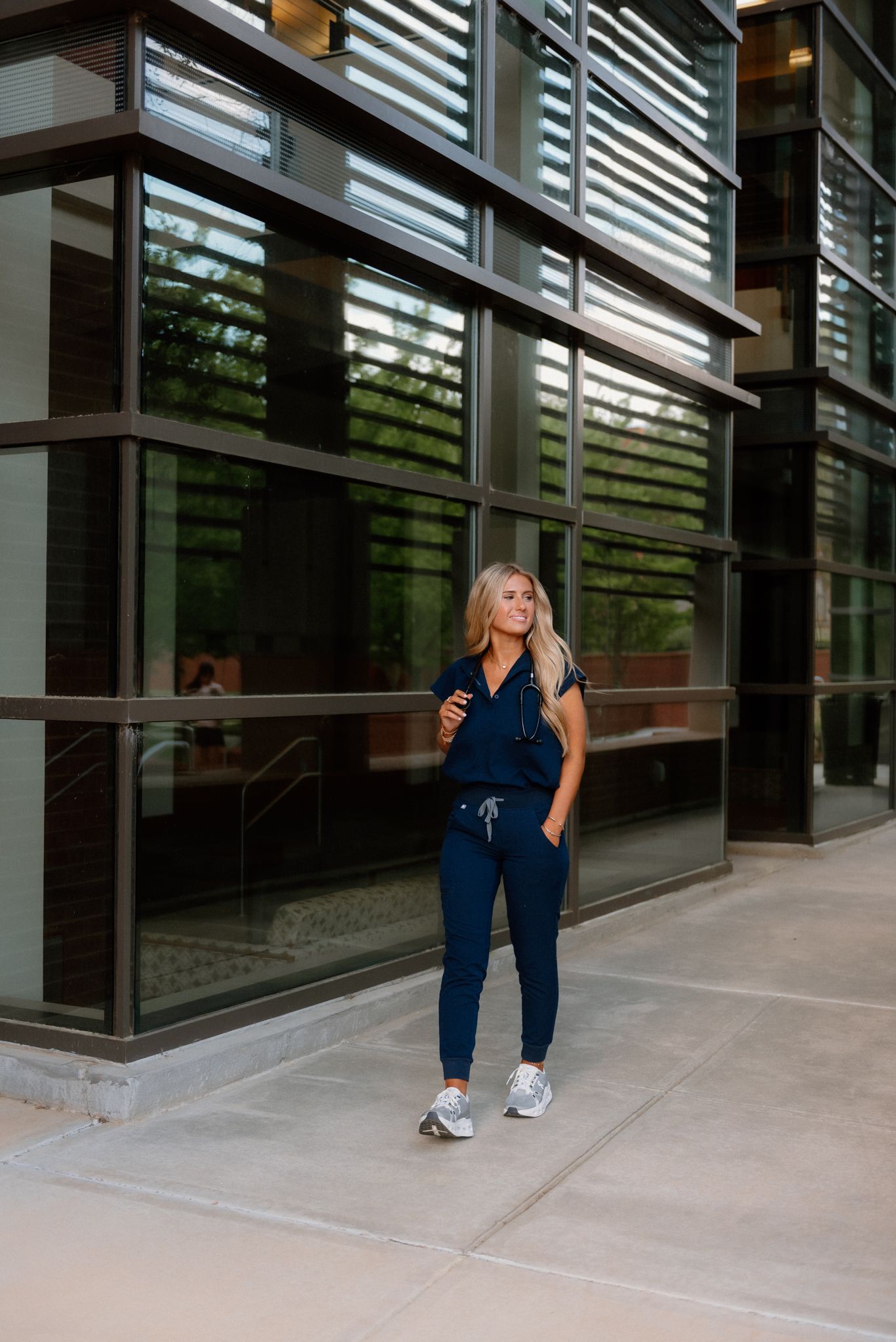 Athletic figure in navy blue athleisure outfit with coffee cup stands outside modern glass office building.