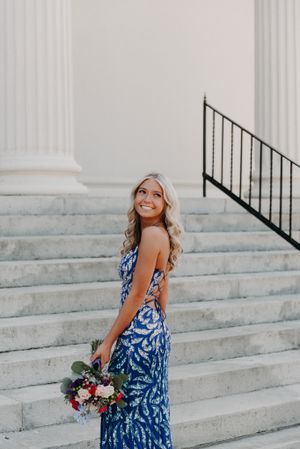 Woman in blue floral dress poses with bouquet on elegant white stone steps.