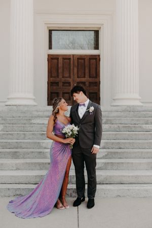 A couple shares a romantic moment on church steps, with the bride wearing a sparkly purple gown and holding a white bouquet.