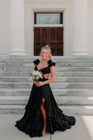 A stunning black formal gown with a leg slit and cap sleeves on the steps of a classic columned building.