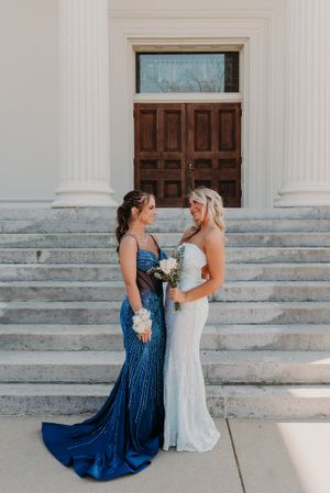 A wedding scene on grand stone steps with two figures in elegant gowns - one in royal blue and one in white.