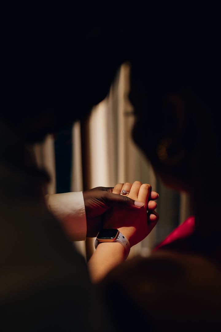 Artistic close-up shot of clasped hands with wedding rings in dramatic lighting.