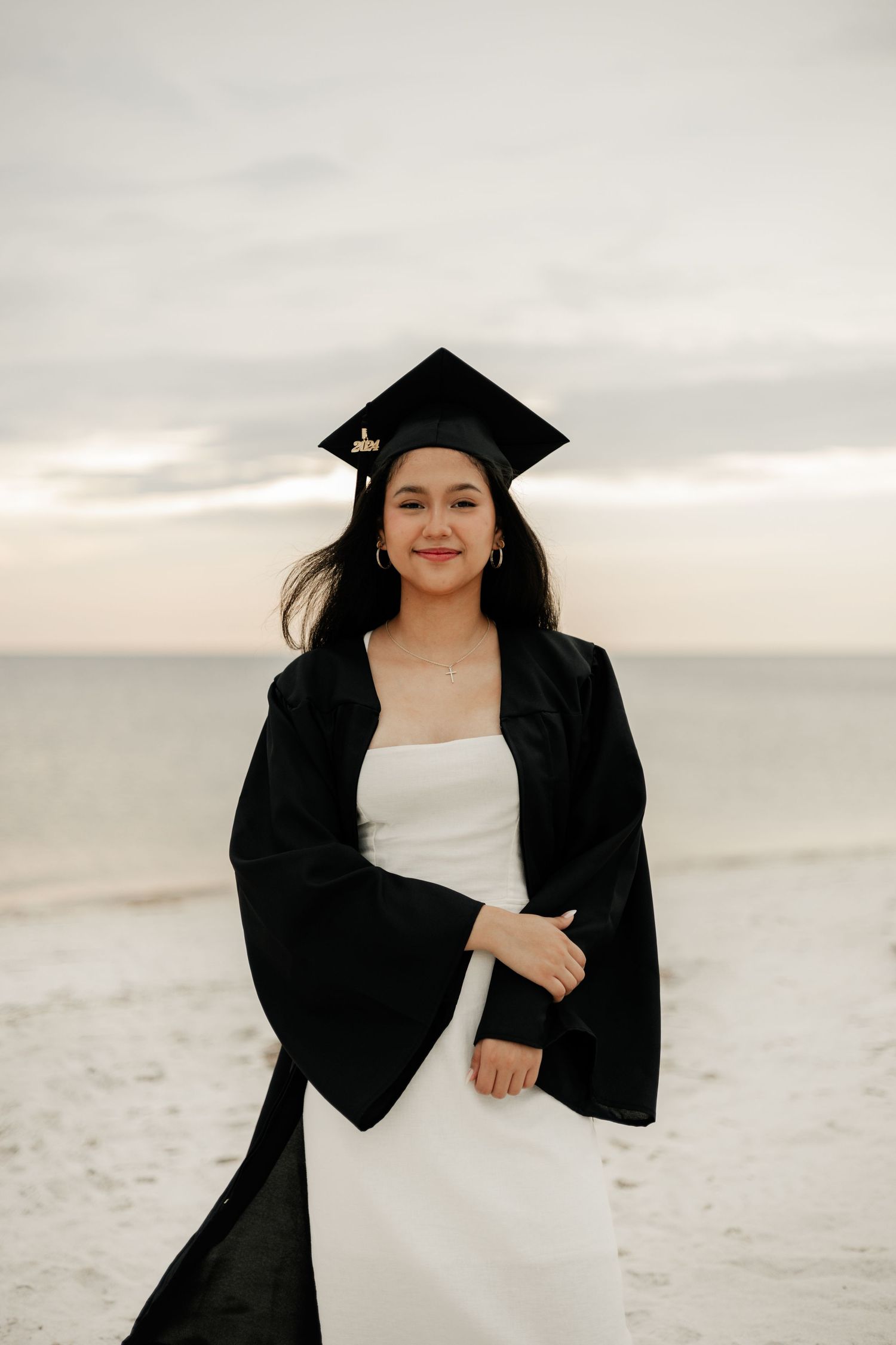A graduate in black cap and gown poses joyfully on a beach during sunset in a series of candid shots.
