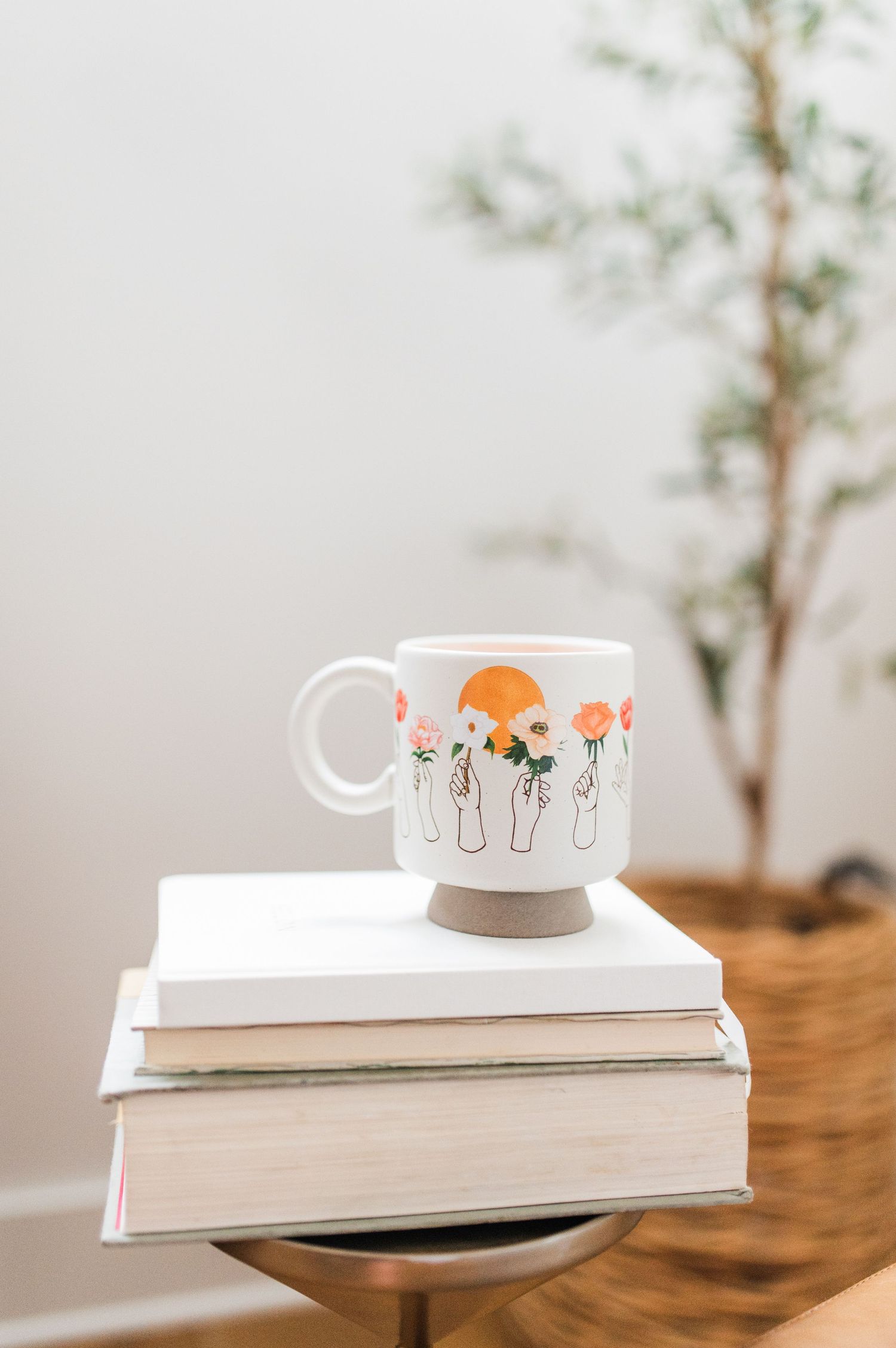 A coffee cup placed on top of stacked books against a neutral backdrop, creating a cozy and minimalist aesthetic.