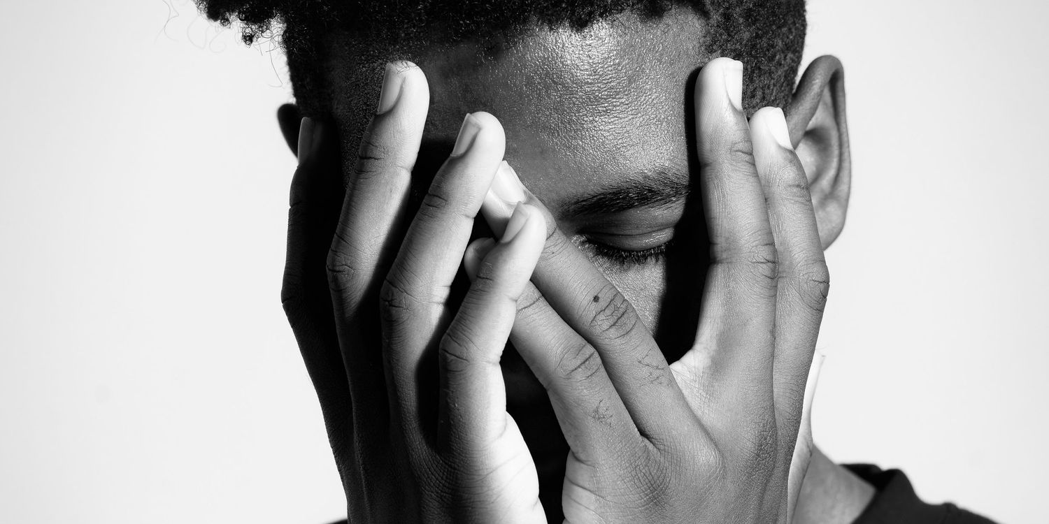 Dramatic portrait of a young black man holding his face in his hands against a white background