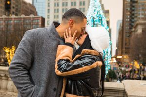 After proposal, couple kisses and show off the new ring in front of Christmas tree in millenium park Chicago