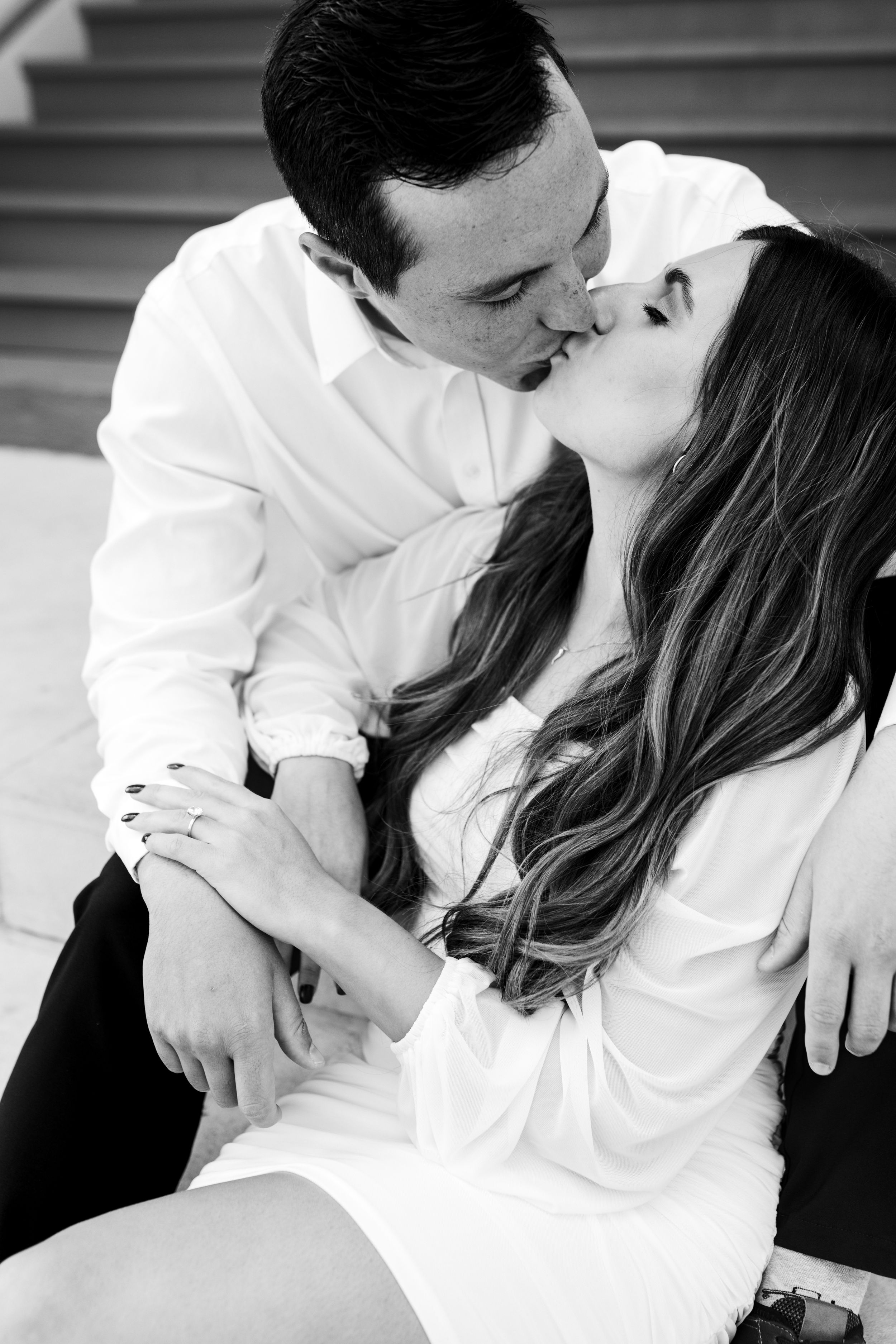 Man and woman embrace on stairs and kiss. black and white image. engagement ring in focus