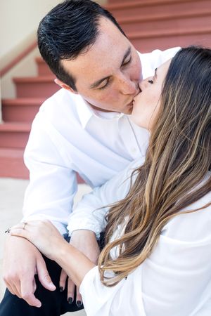 engaged man and woman kiss on stairs outside.