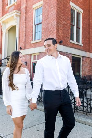 Man and woman in dress clothes. Woman in white walk down street in Illinois holding hands and looking at each other