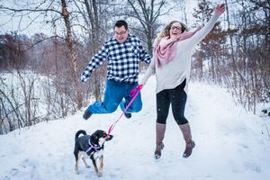 Couple jumps for joy in the snow with dog at minneapolis minnesota park