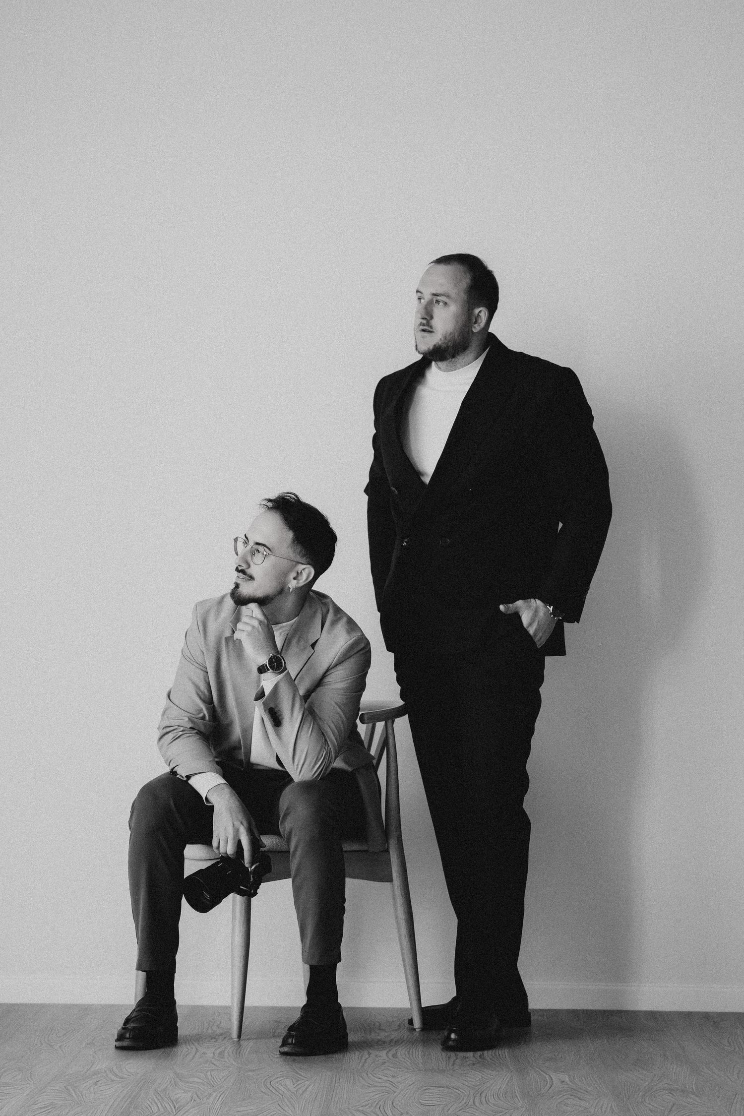 Two people in business attire posing against brown background in studio setting.