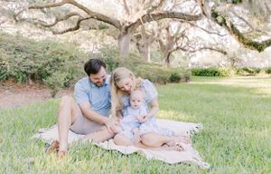 A family picnic scene on a blanket under Spanish moss-draped trees in a park setting.