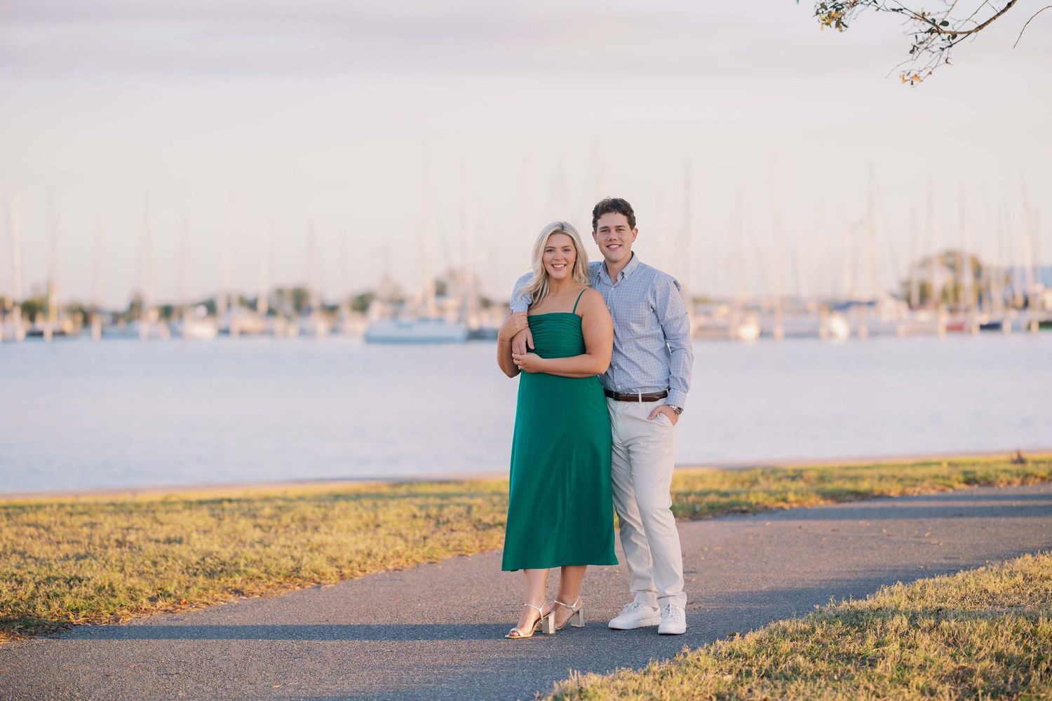 Couple stands together on waterfront path during sunset.