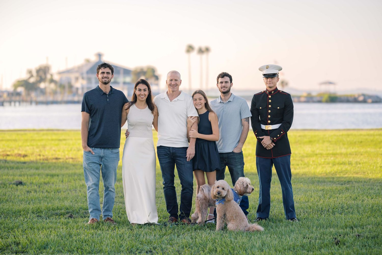 Family group portrait with dog on grassy waterfront with military service member present.