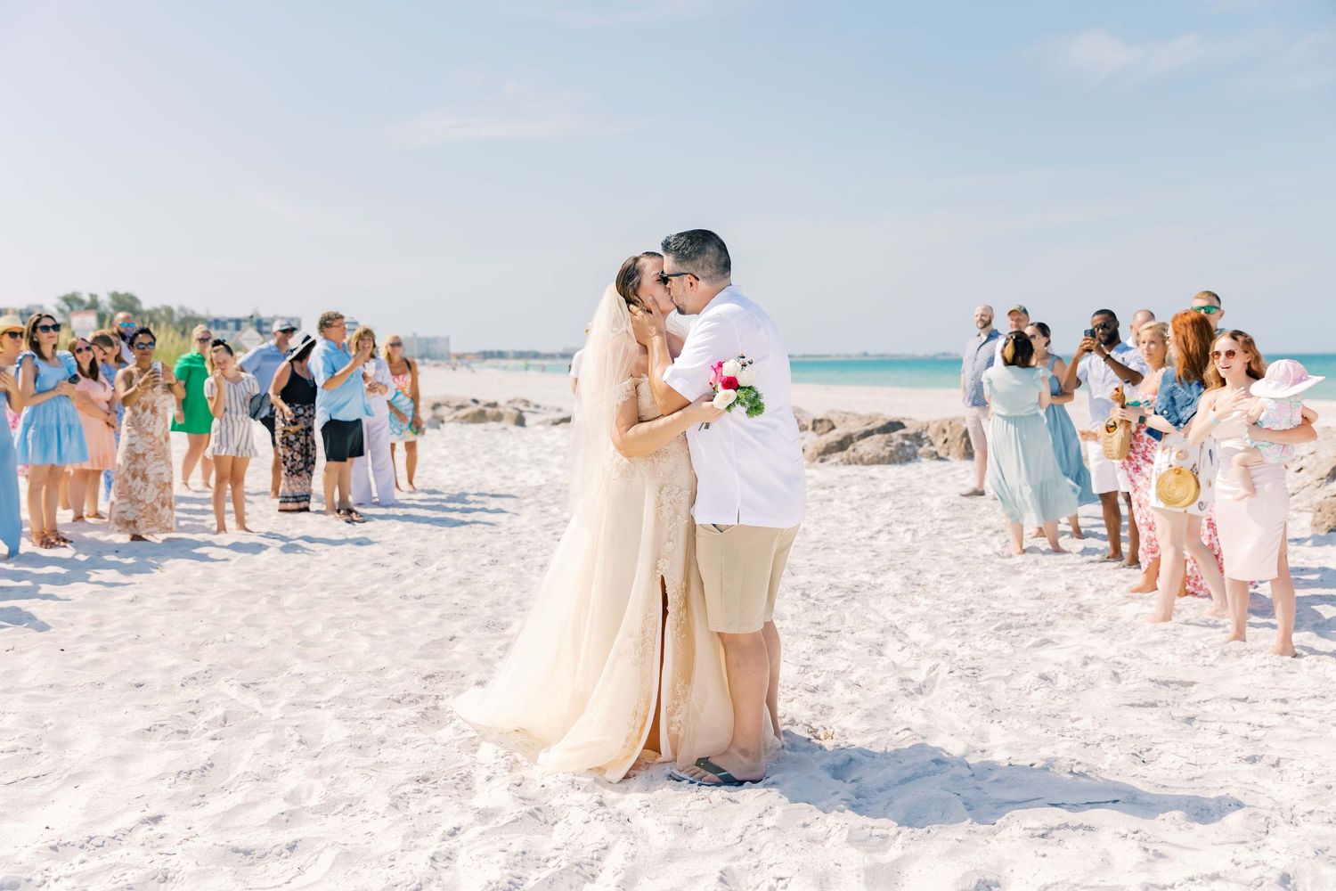 Wedding ceremony on a sunny beach with guests watching the couple's special moment.