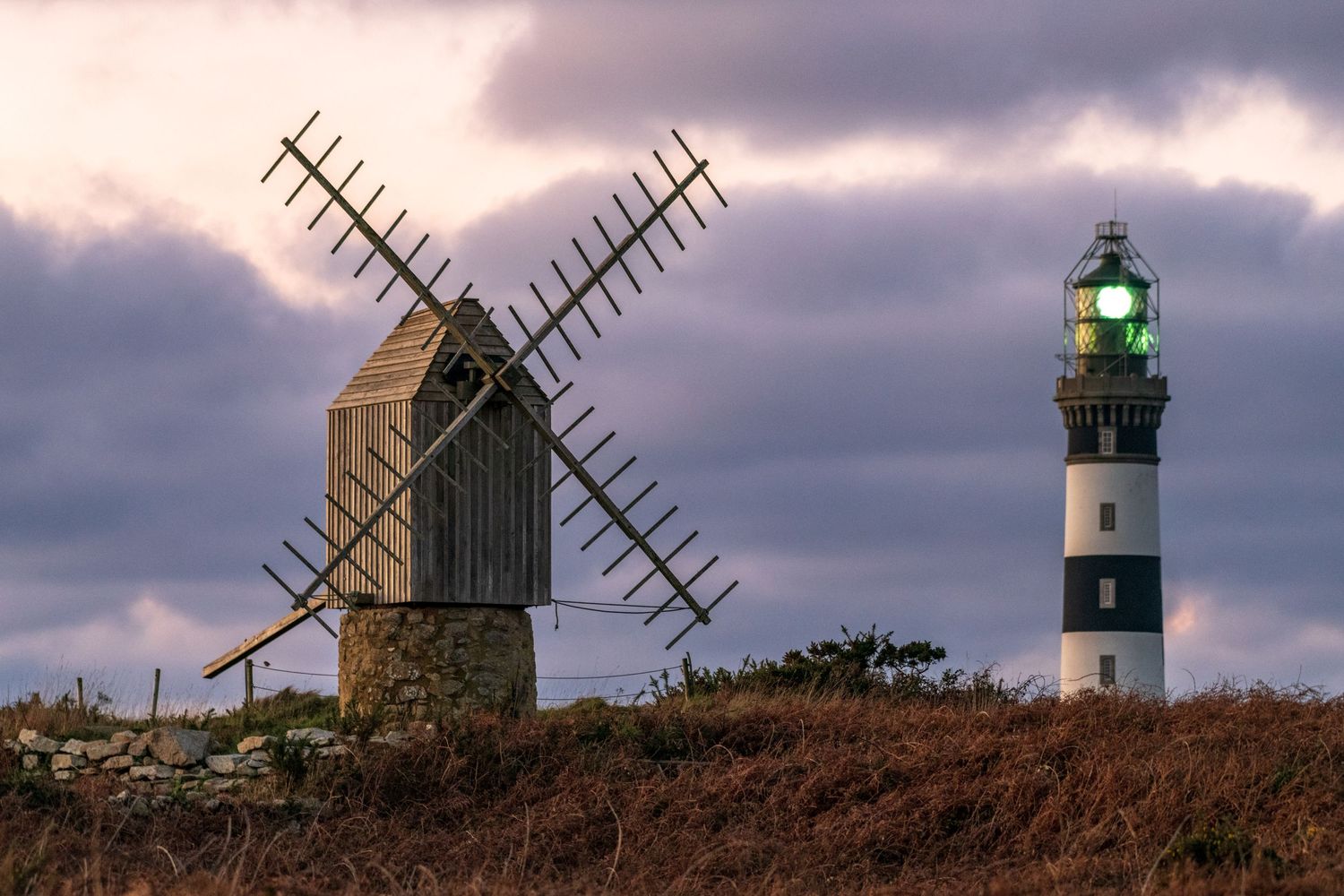 Scenic view of a lighthouse and windmill silhouetted against a dramatic purple sunset sky.