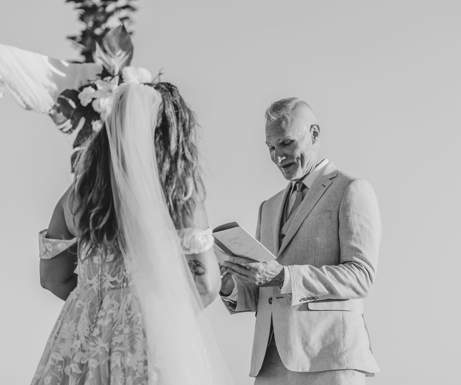 A black and white wedding ceremony photo capturing a moment under an outdoor arch.