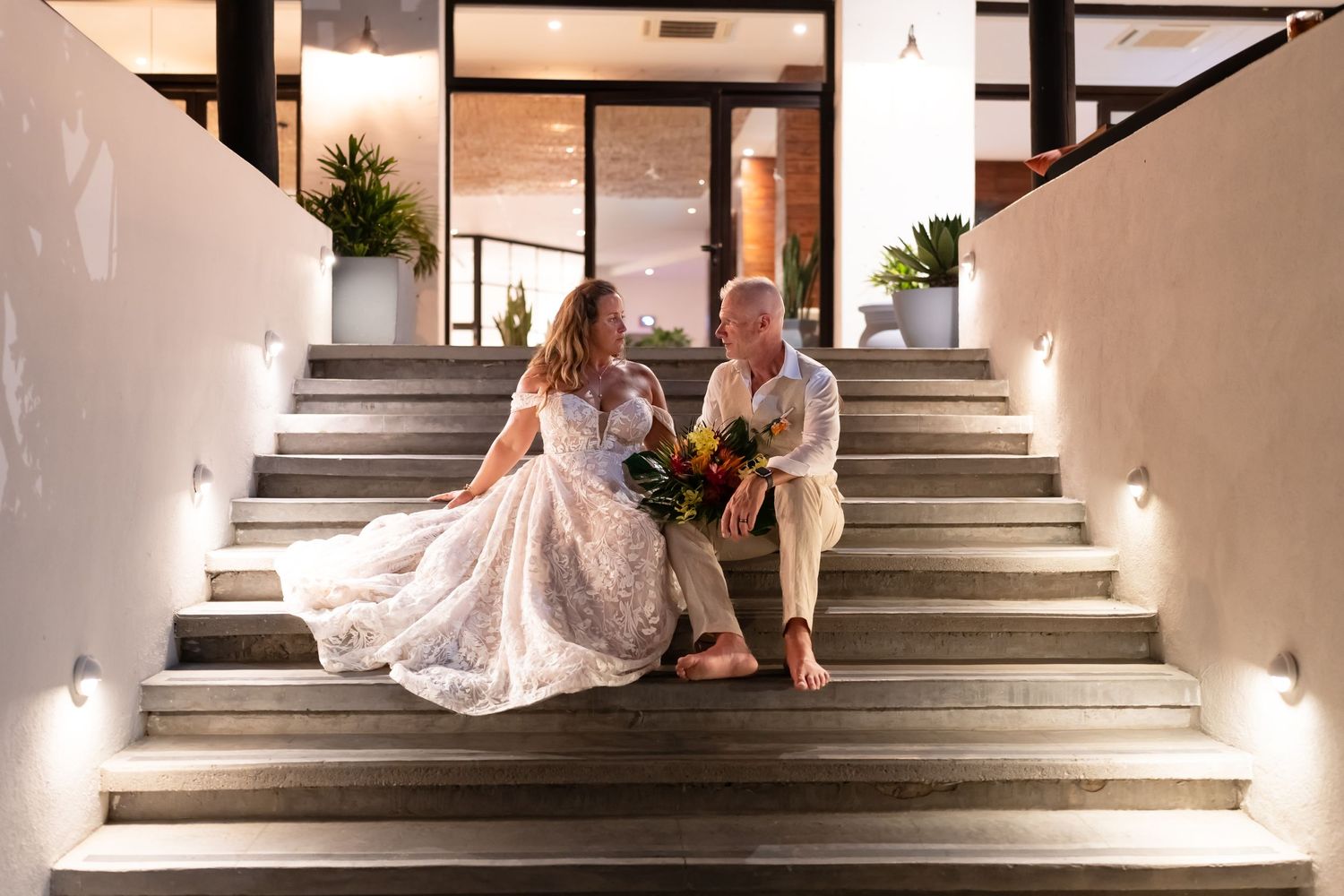 A wedding couple sits together on illuminated steps in an elegant indoor venue.