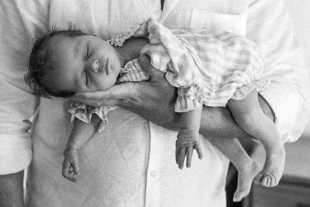 Black and white photo of father cradling sleeping newborn baby in arms.