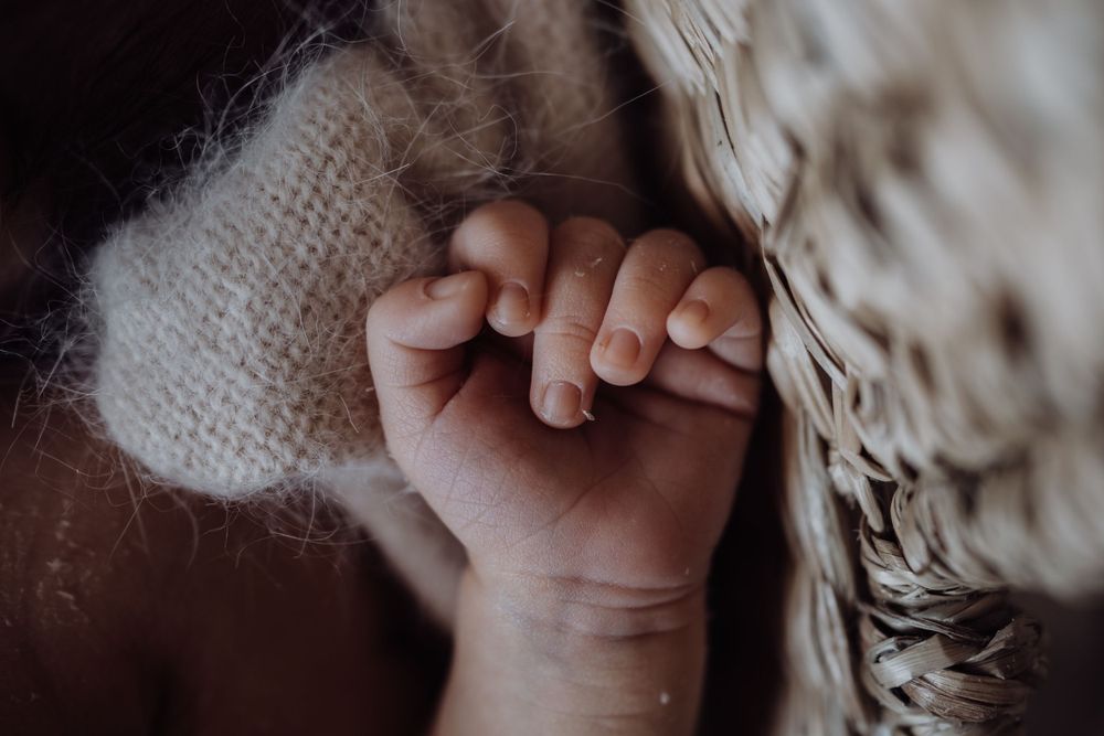 Extreme close-up of tiny newborn baby fingers and fist against soft knit blanket.