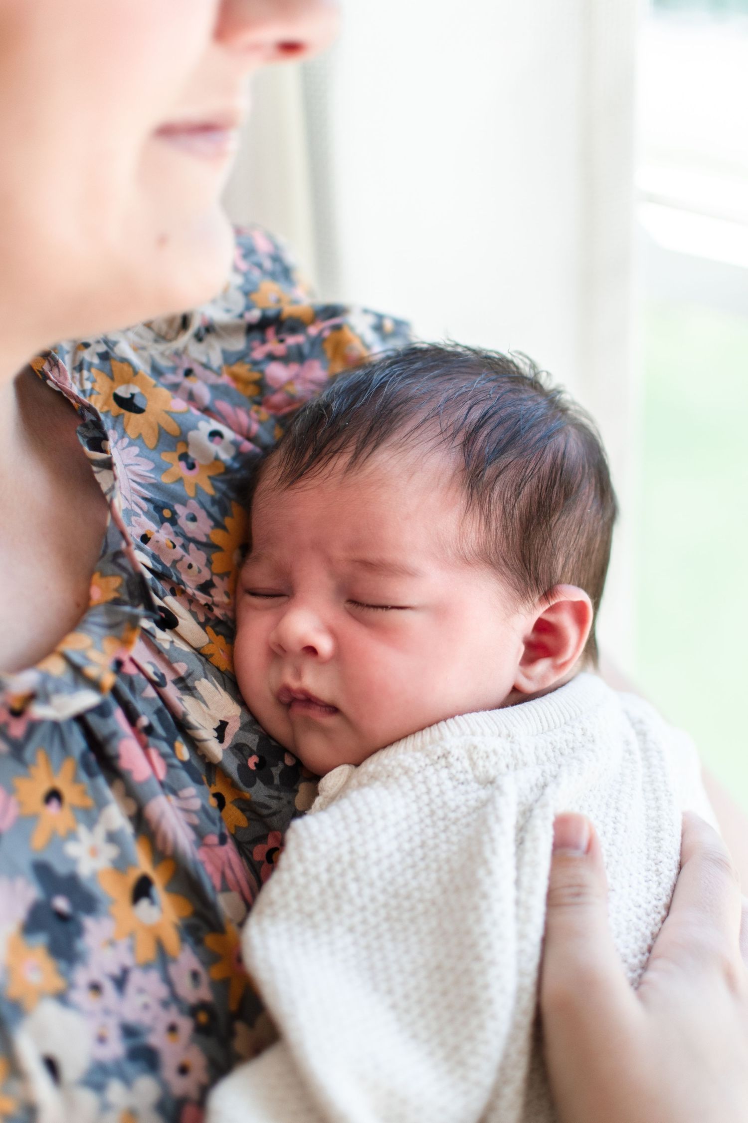 Sleeping newborn wrapped in white blanket resting against floral pattern.