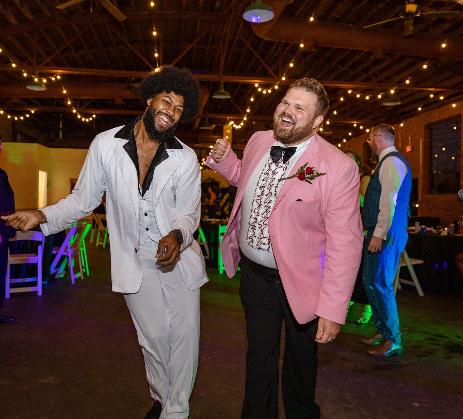 Two partygoers dance and celebrate in an indoor venue decorated with string lights.