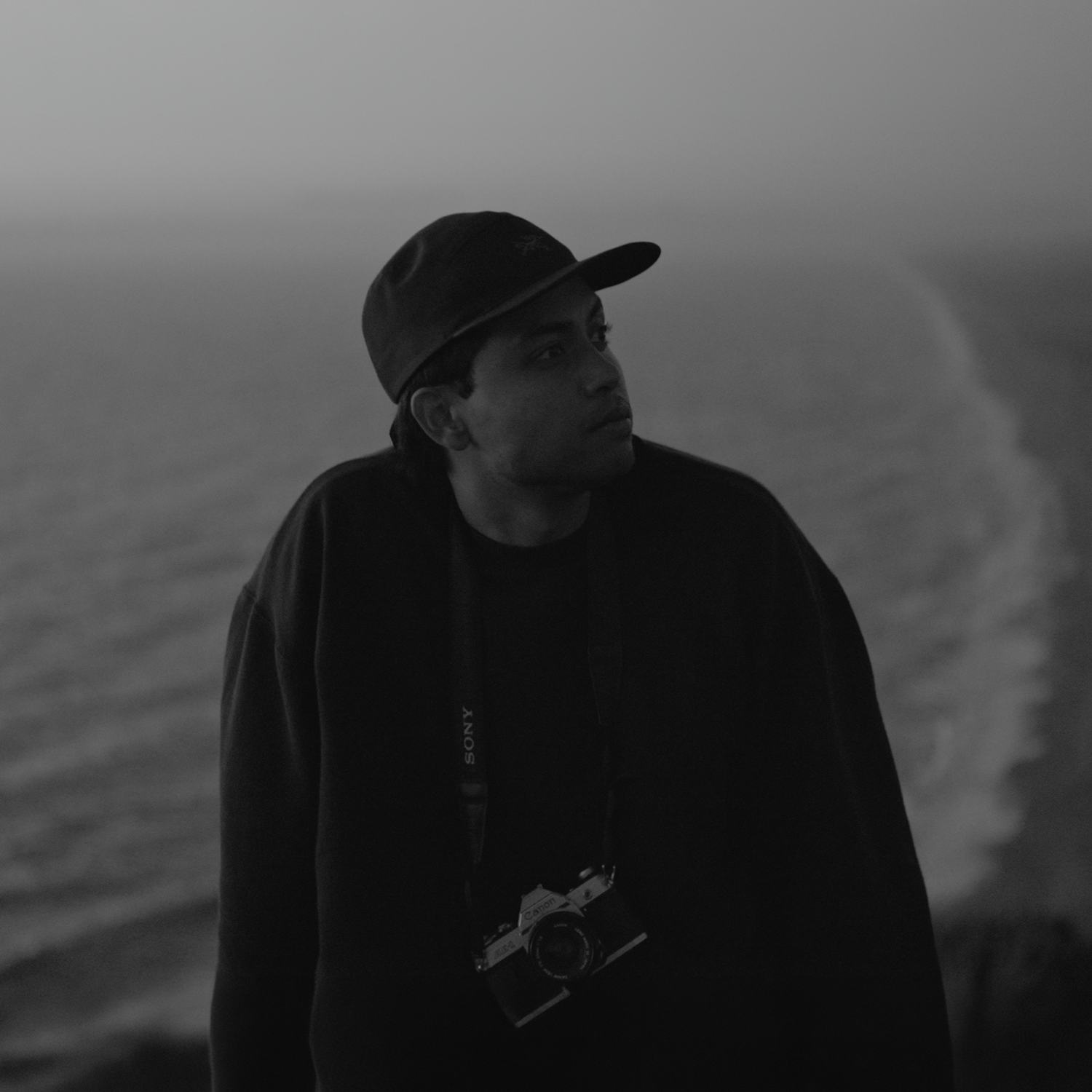 Person in dark clothing silhouetted against coastal cliffs and ocean at sunset.