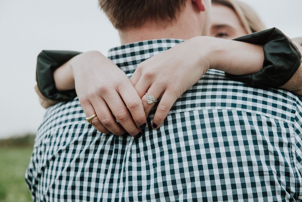 close up of engaged couple and showing engagement ring over mans shoulders