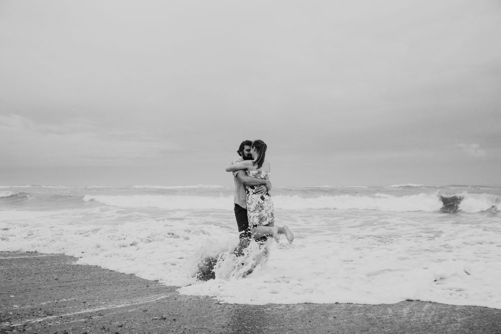 couple hugging and laughing while a wave crashes into them on a West Coast beach