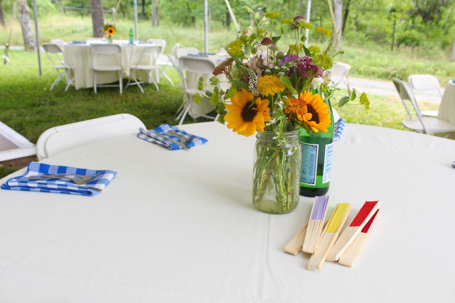 An outdoor table setting with sunflower centerpiece, blue napkins and wooden utensils.