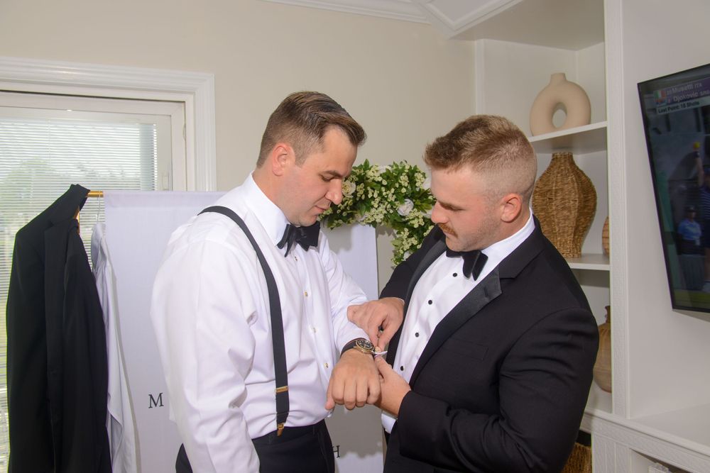 Groomsman helps groom with cufflinks while getting ready for the wedding ceremony.
