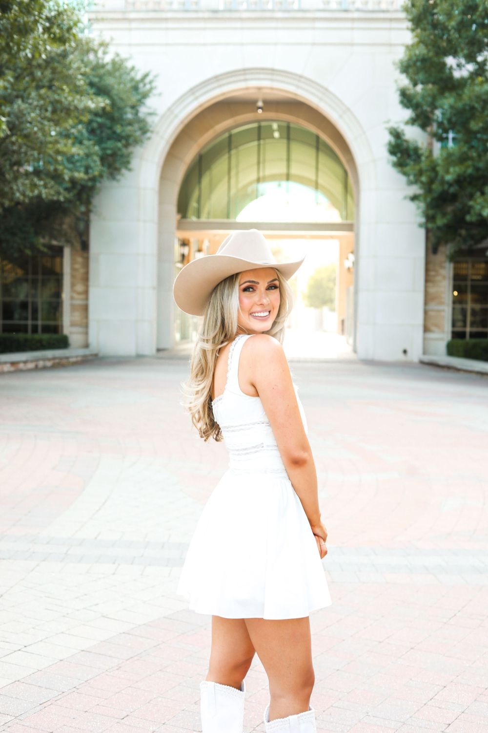 A series of fashion photos showcasing a summery white dress and beige hat ensemble in front of arched architecture.